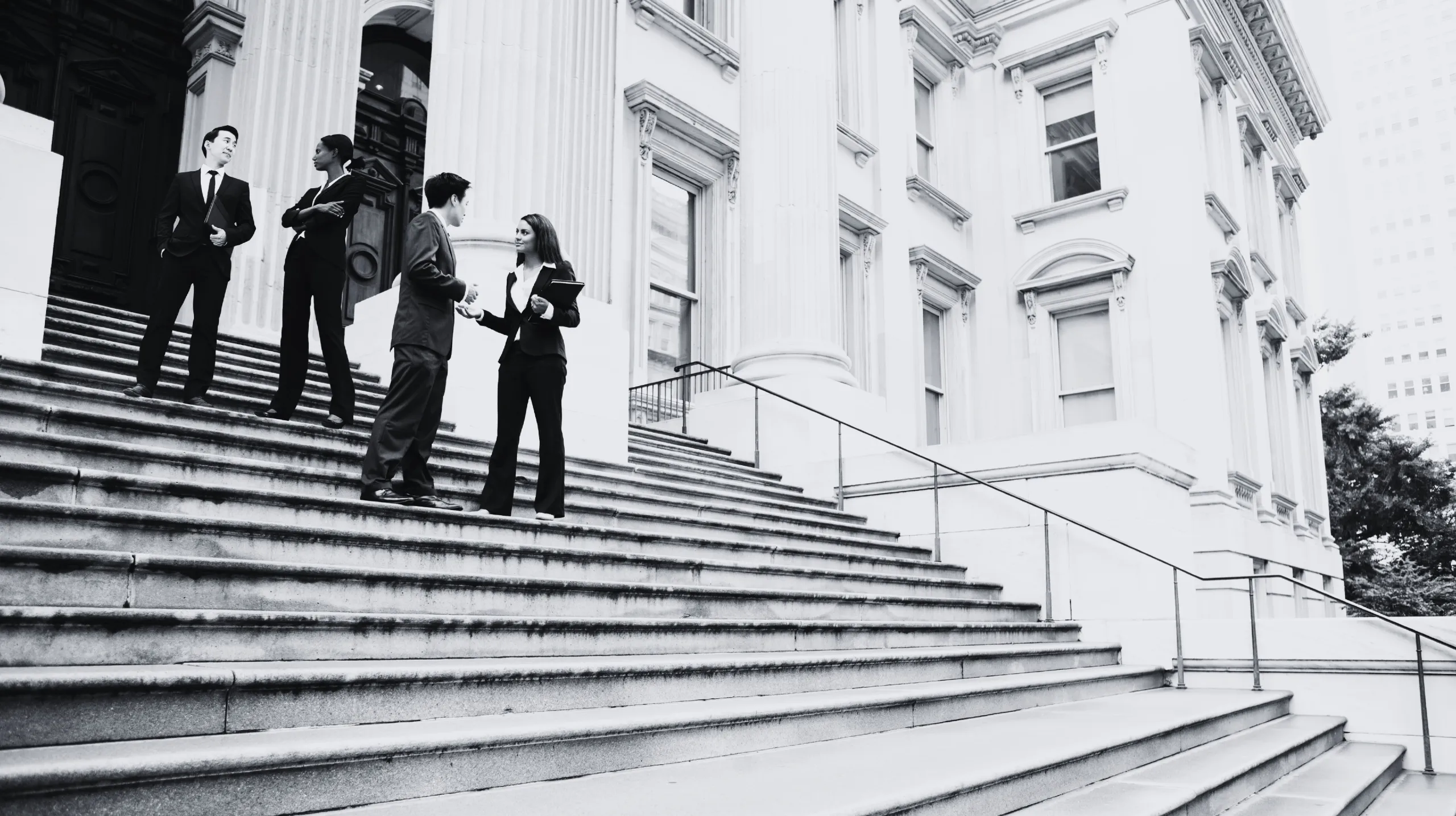 Slide 3 - Individuals in suits conversing on stairs in front of a big building